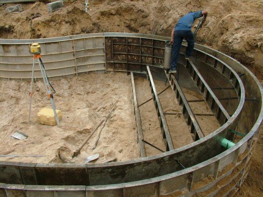 Concrete step forms set first inside a radius pool wall, with a laser level on its tripod