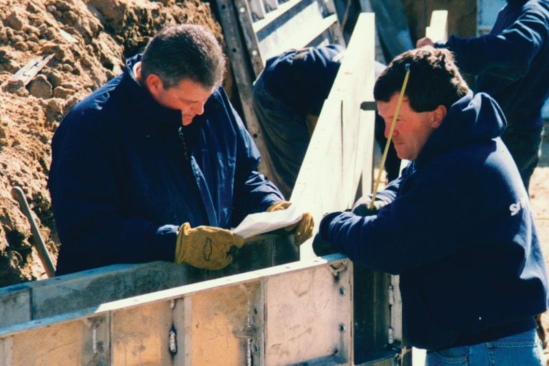 Two crew members working at the top of a pool wall form on a jobsite