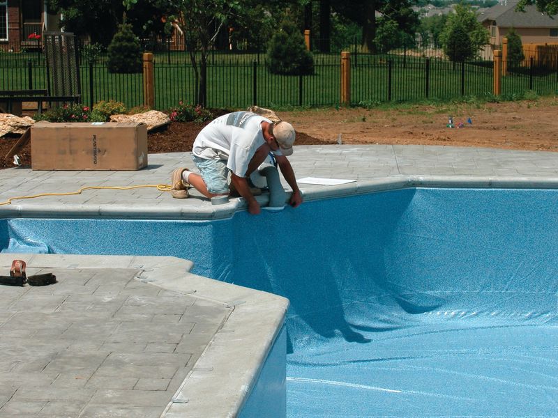 Installer at the pool edge fitting a vinyl liner bead into the liner track