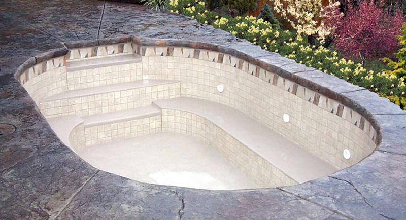 Oval concrete spa with a bench, set in a stamped concrete deck