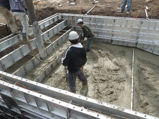 Crew placing concrete into the deep end wall forms from a pump hose