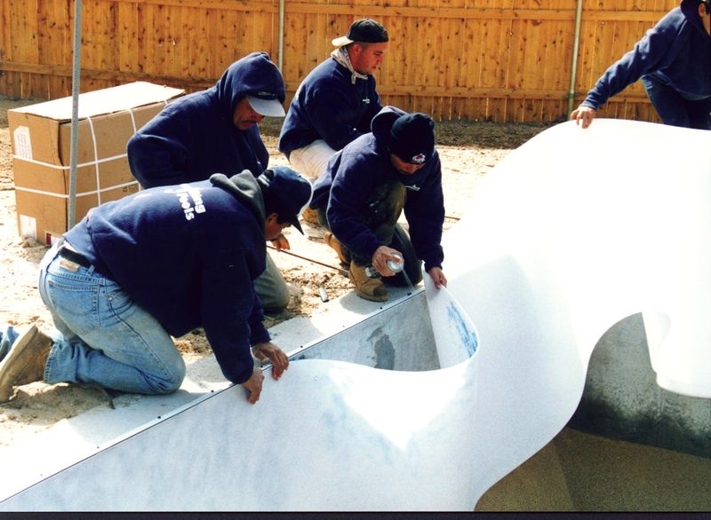 Crew spraying adhesive and fitting foam on the pool wall and floor